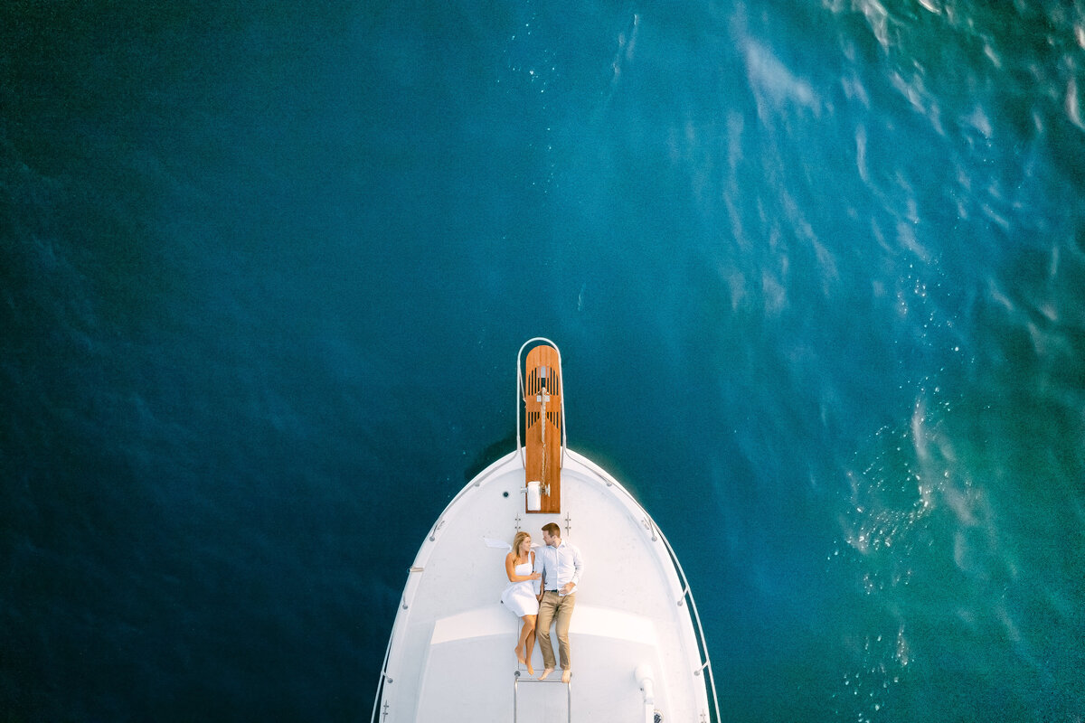 Aerial of a couple on a yacht bow over teal water