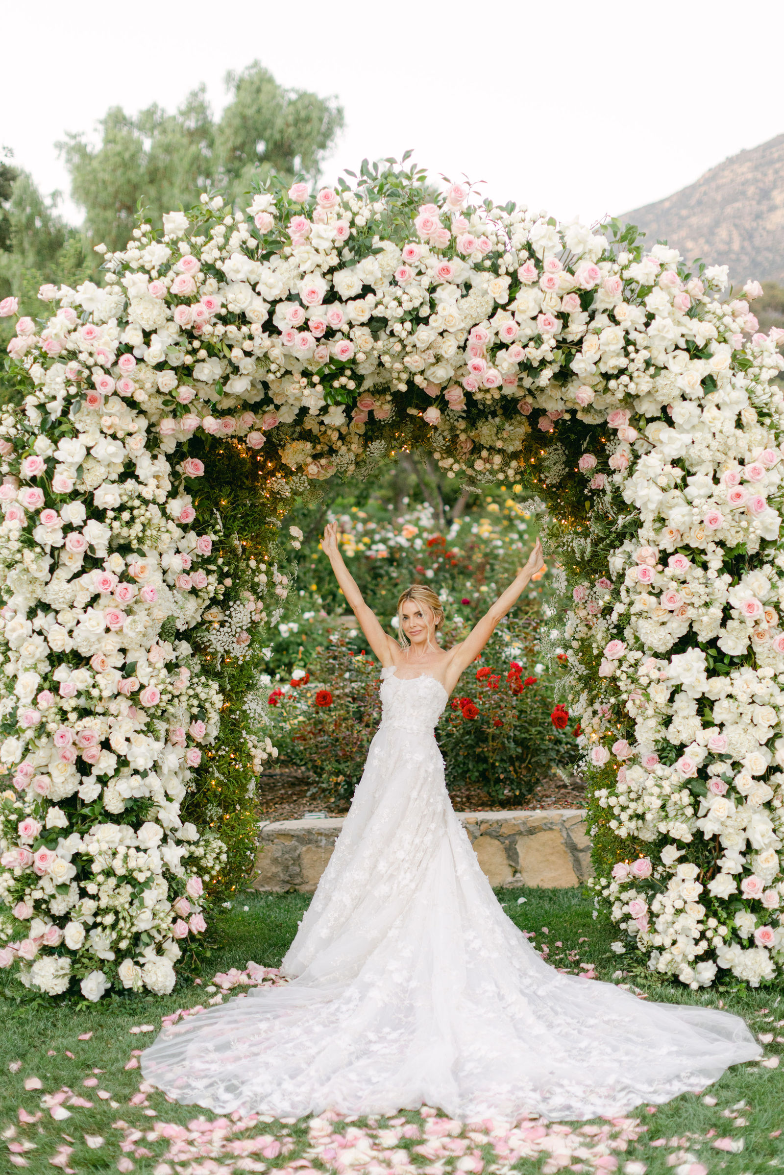 Sofia, arms up beneath the rose arch